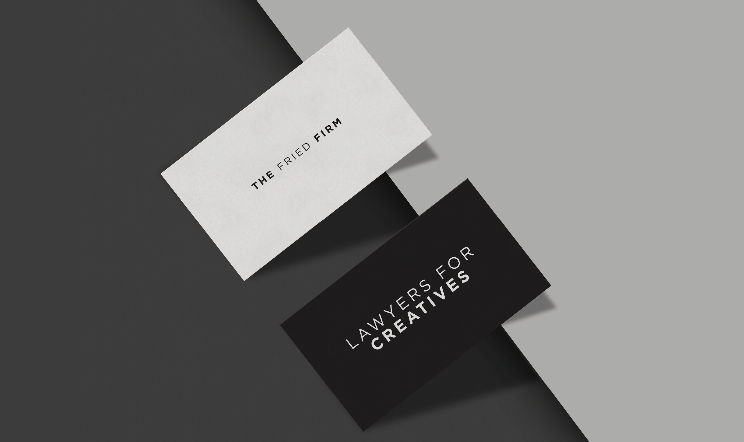 Two business cards placed diagonally on a split-tone background—light gray on the right, dark gray on the left. The upper card is white with black text reading 