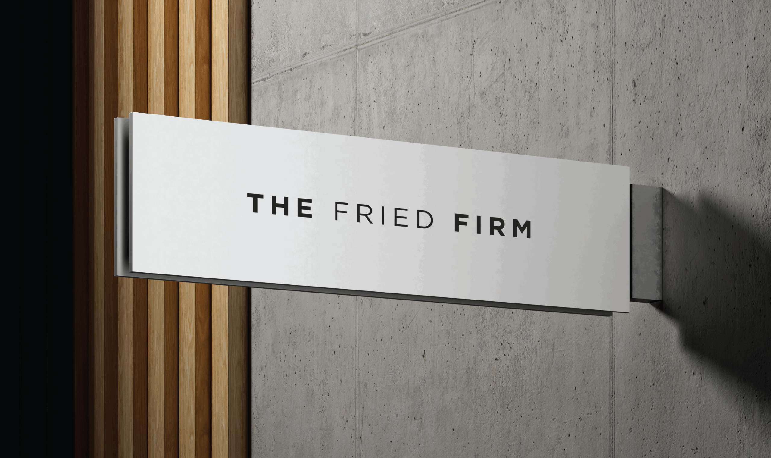 Wall-mounted sign with bold black text reading “THE FRIED FIRM” on a white background, attached to a concrete wall beside vertical wooden slats.
