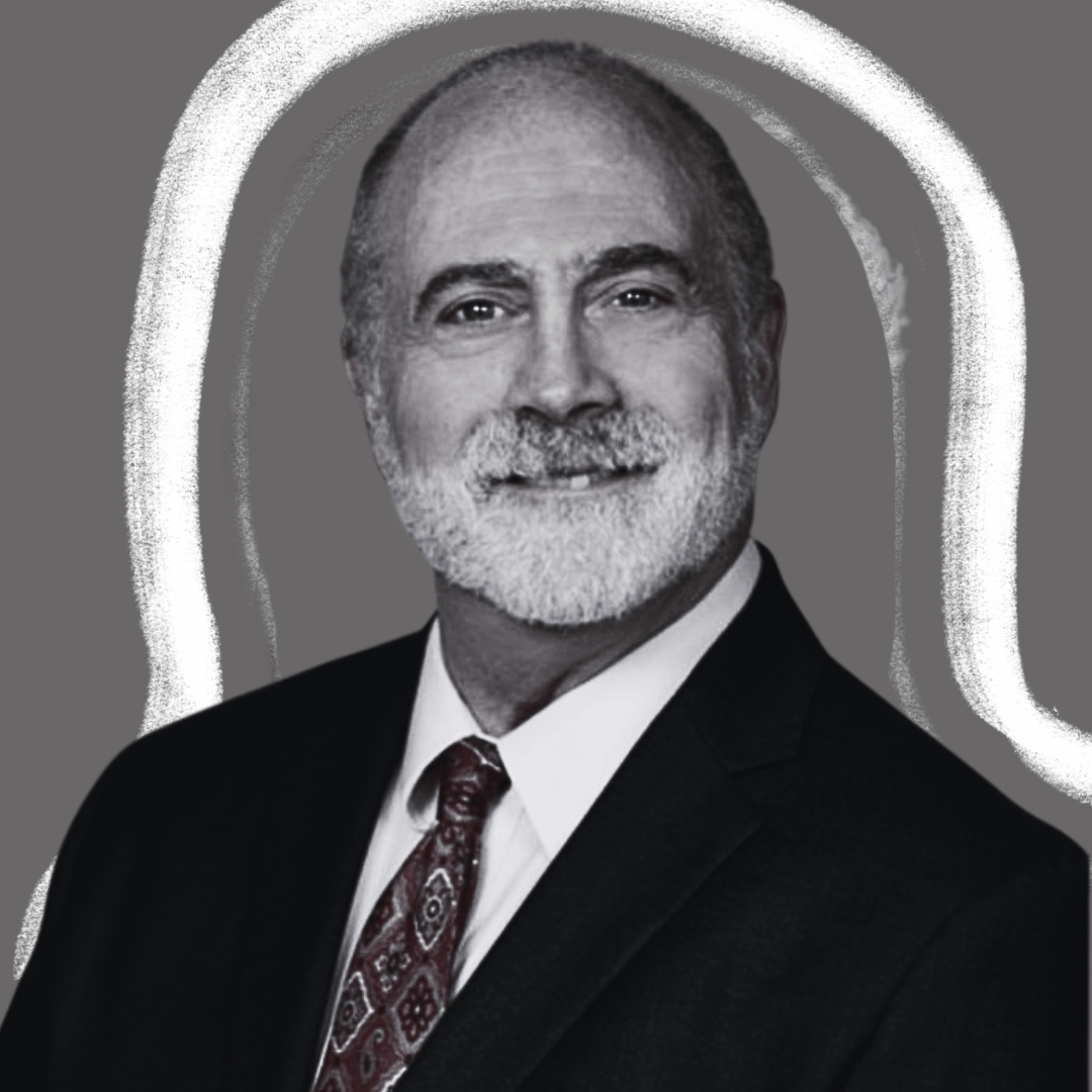 A smiling older man with a white beard and mustache wears a suit and patterned tie, posed against a gray background with white curved lines drawn around him.