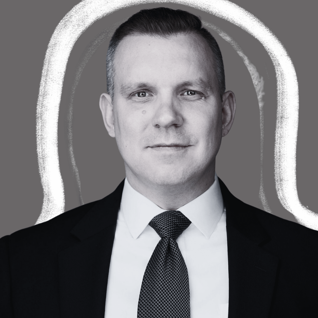 A man in a black suit and patterned tie looks directly at the camera against a gray background with white, hand-drawn arches framing his head.