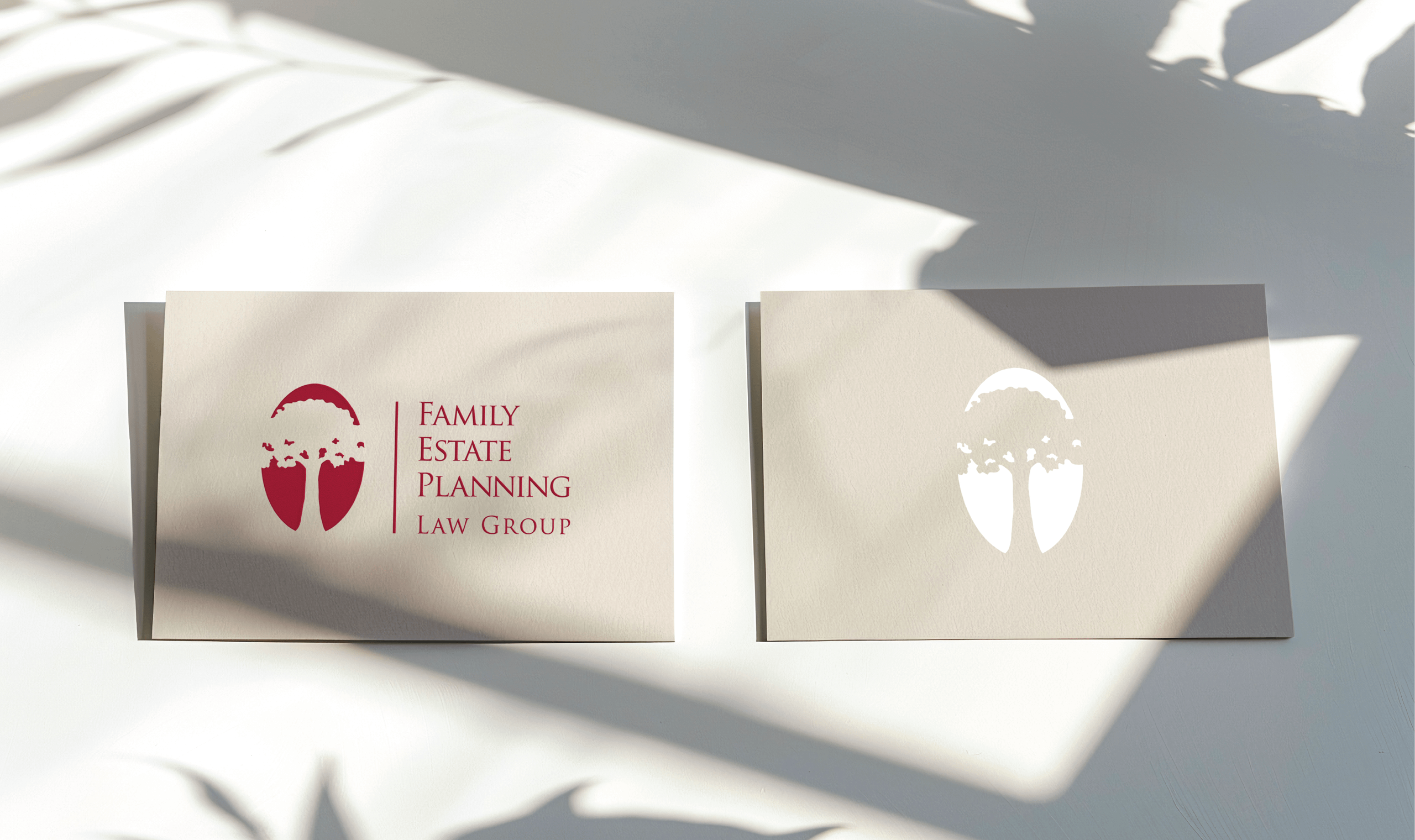 Two business cards on a light surface, partially shaded by plant shadows. The left card features a red 