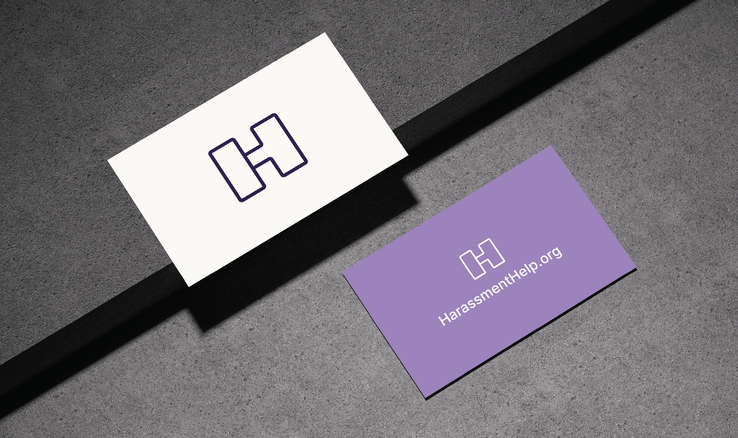 Two business cards on a textured gray surface. The cream card has a bold 