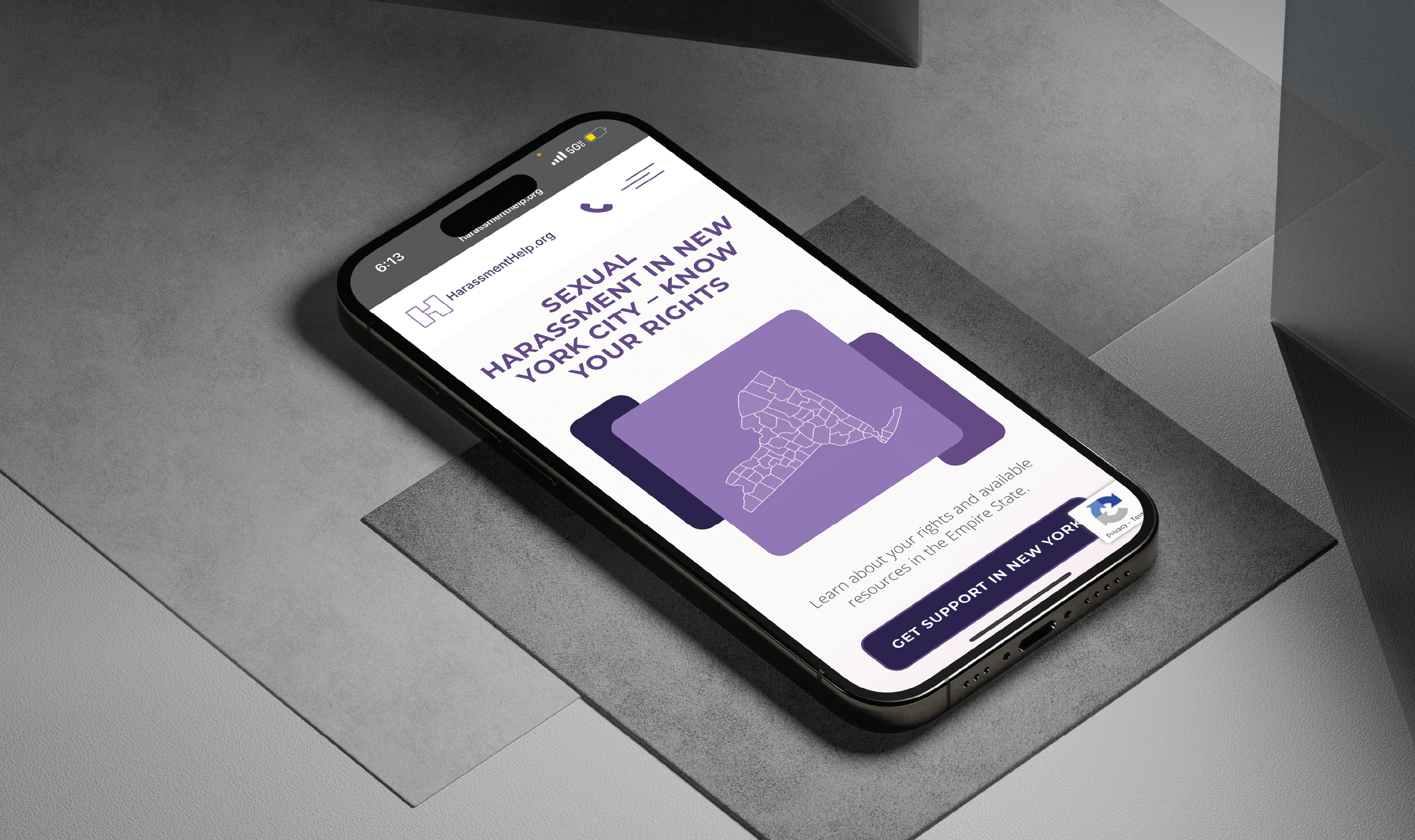 A smartphone on a gray surface displays the HarassmentHelp.org website about sexual harassment awareness in New York City, emphasizing knowing one's rights.