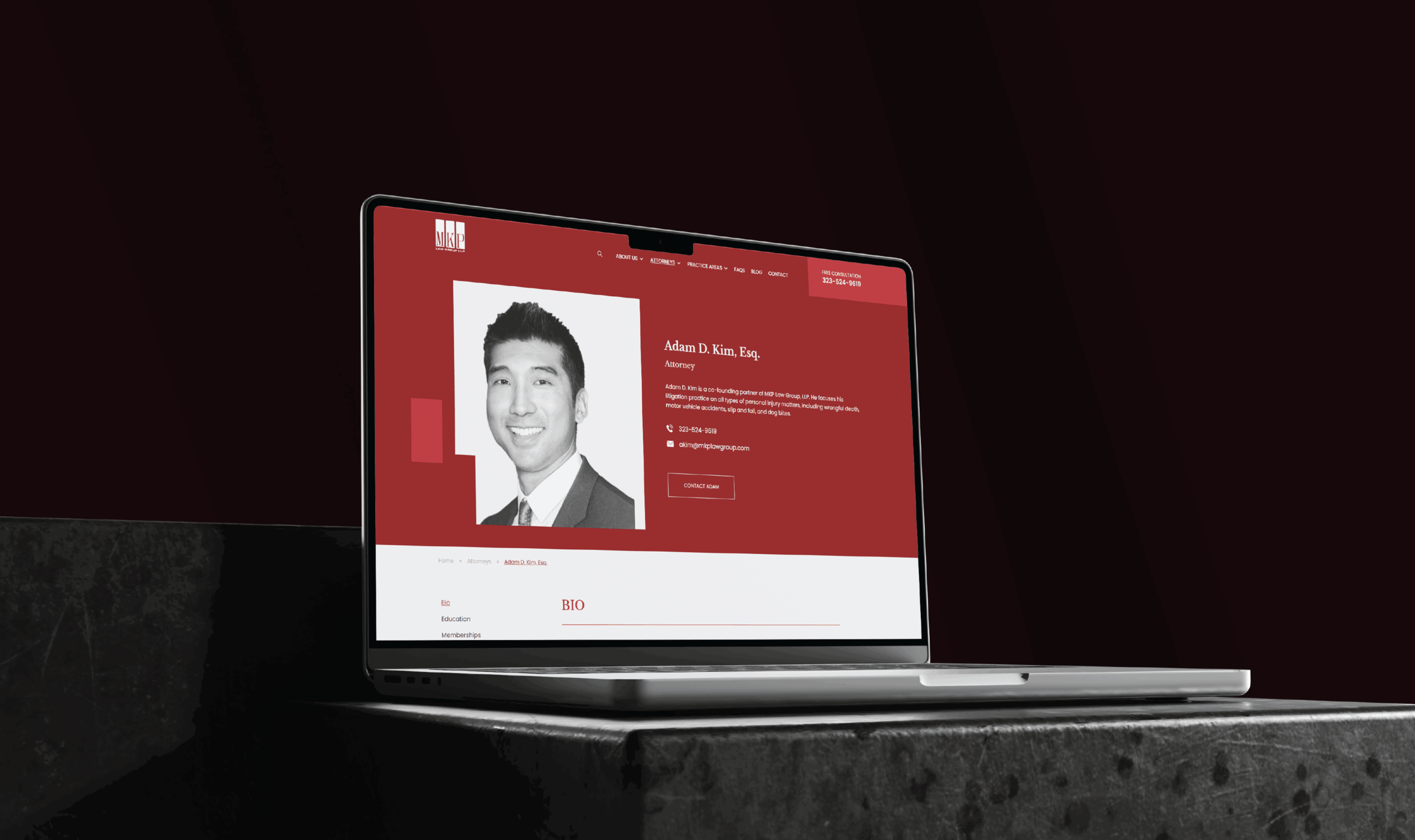 A laptop on a dark stone surface displays the MKP Law Group's redesigned website with a red and white theme. The screen shows a profile photo and contact details.