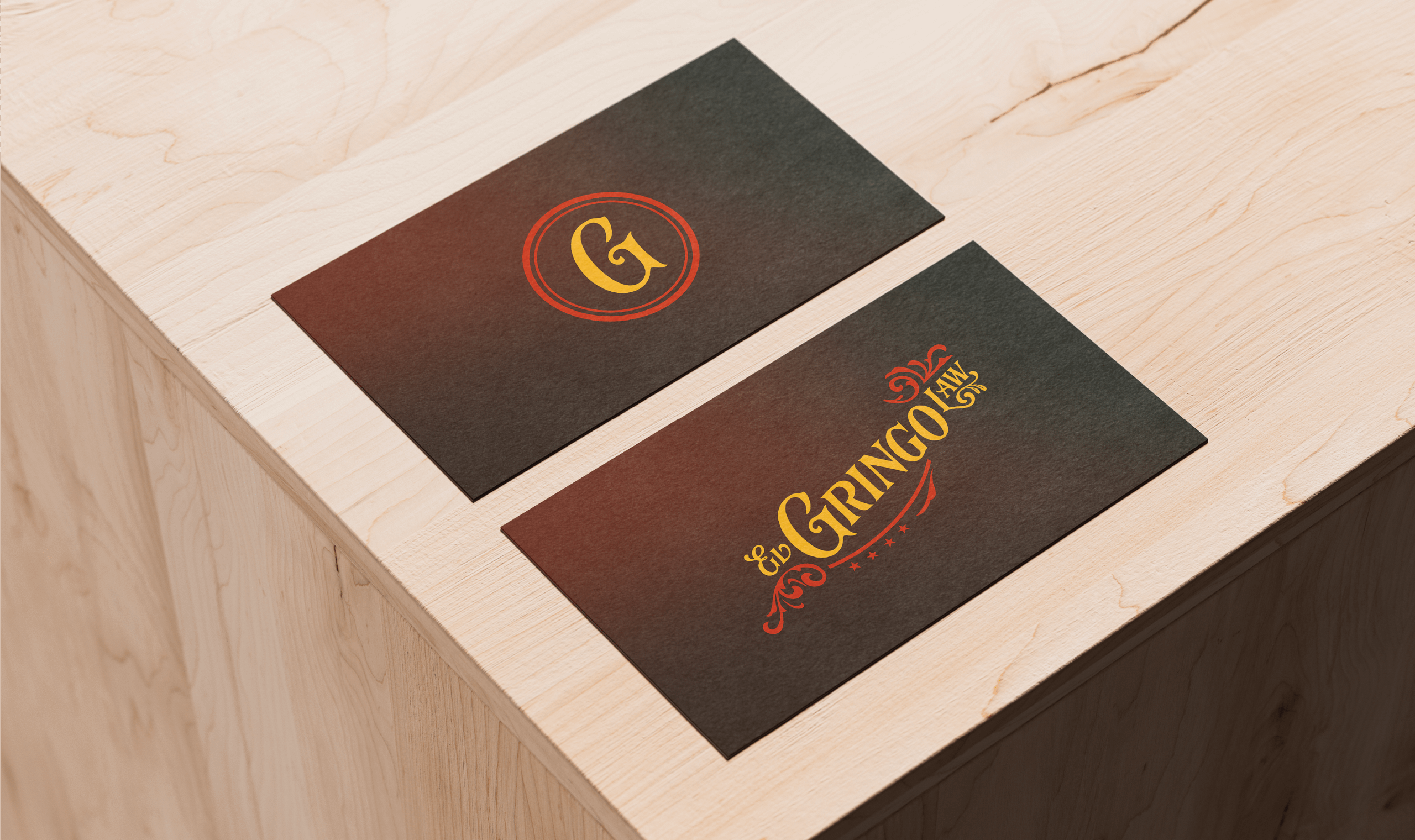 Two elegant business cards placed on a light wooden surface. One card displays a stylized 