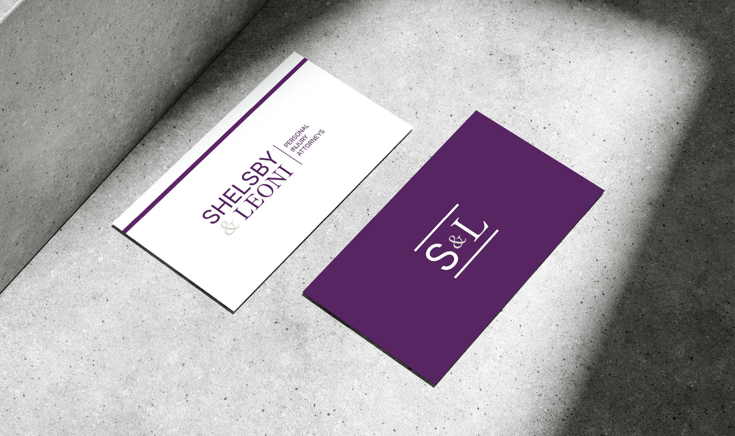 Two business cards on a concrete surface. The left card is white with purple text reading 