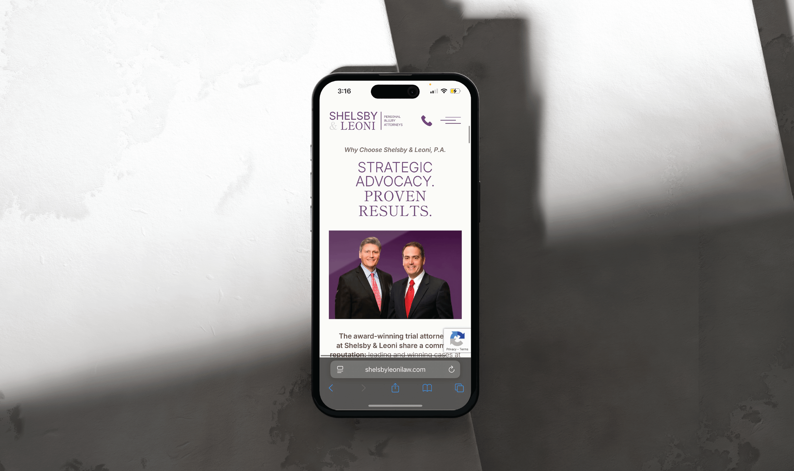 Smartphone displaying the updated Shelsby & Leoni website with the two named attorneys in suits, one gray-haired and one dark-haired, smiling confidently. Text reads 