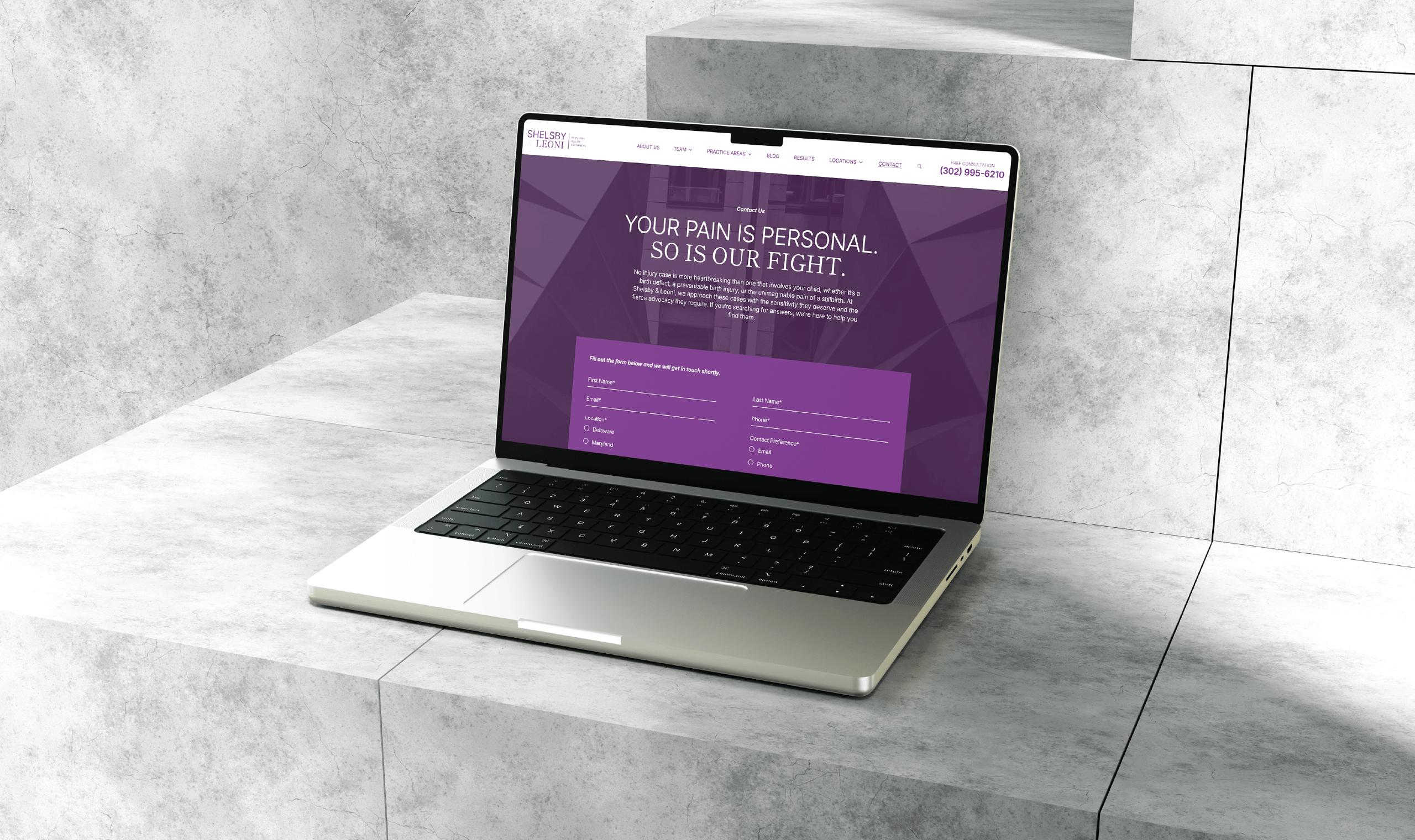 A laptop with a purple-themed Shelsby & Leoni website screen sits on a gray stone step. The website headline reads 