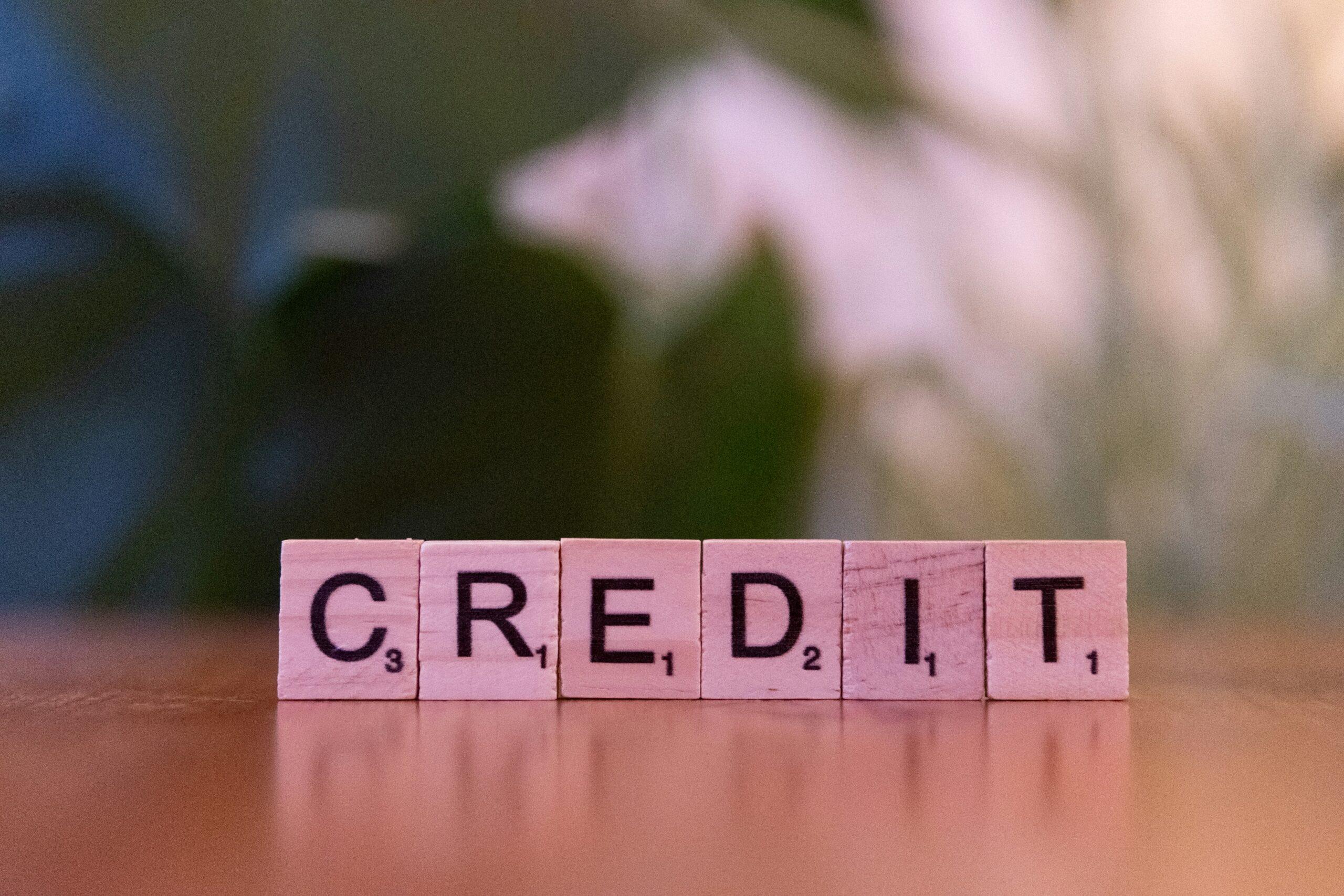Wooden letter tiles arranged in a straight line to spell the word “CREDIT” on a smooth tabletop, with a softly blurred background suggesting an indoor setting.