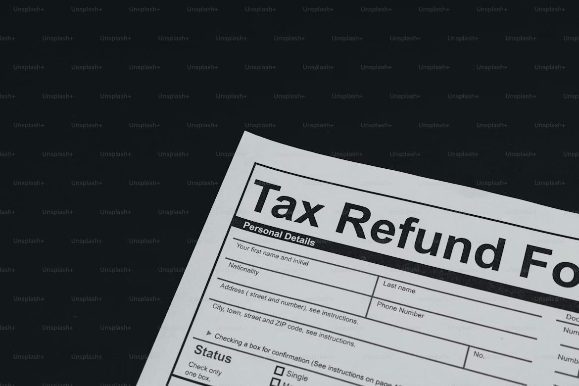 Close-up of a tax refund form angled against a dark background, showing the bold heading “Tax Refund” and sections for personal details, address, and filing status, with most of the page partially cropped and ample empty space surrounding the document.